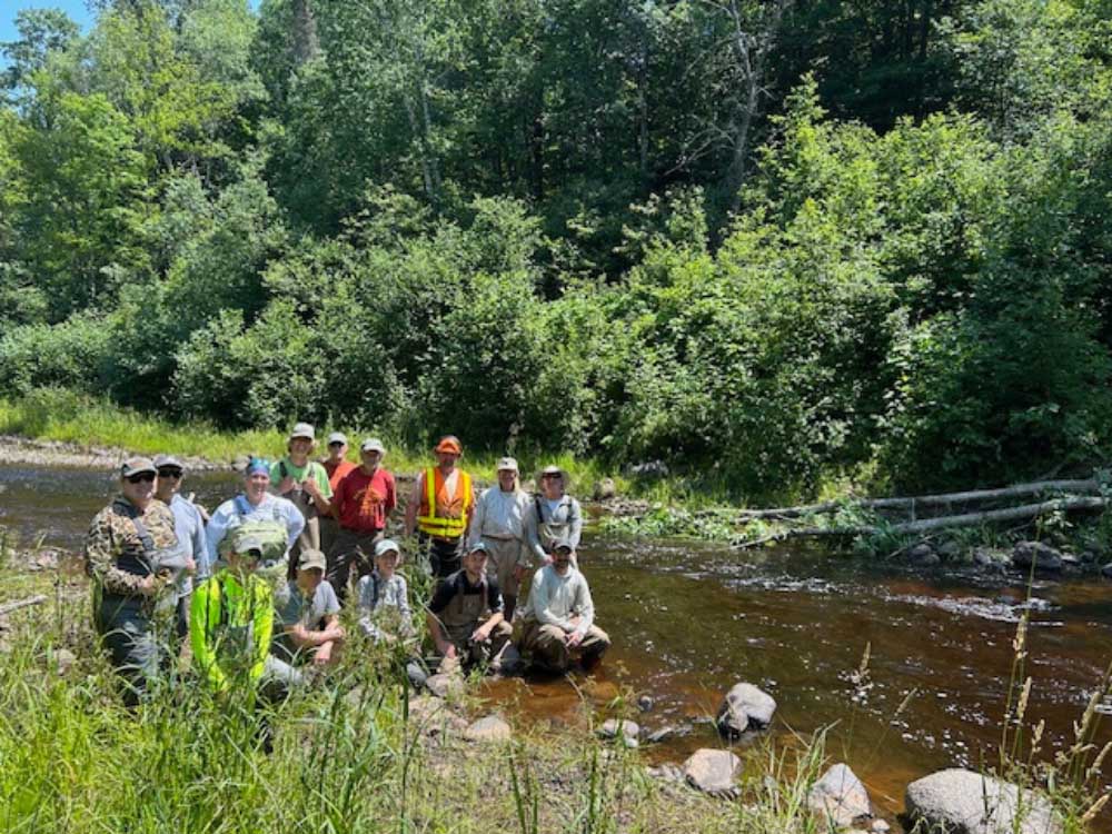 A group of volunteers standing together at the bank of a river. Several of the 22 volunteers who helped move and anchor the large woody debris.